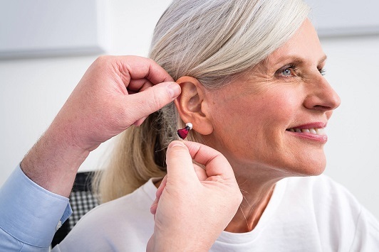 Ältere Frau erhält ein Hörgerät zur Hörverbesserung durch einen Hörakustiker im Ohr.